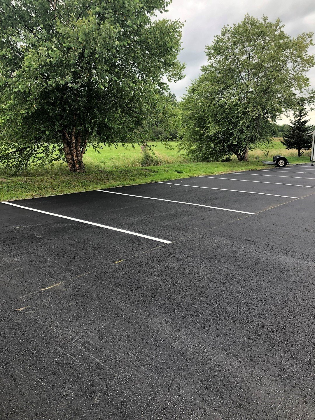 Empty asphalt parking lot beside green trees and grass on an overcast day