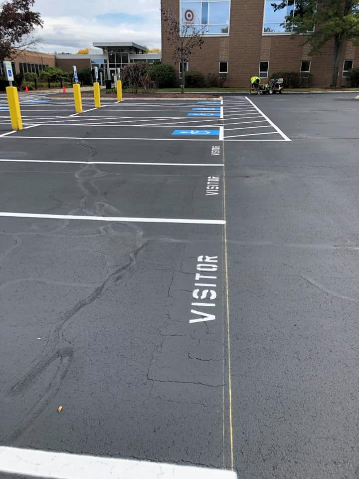 Parking lot visitor spaces with white-striped curb ramp and yellow bollards outside a brick building
