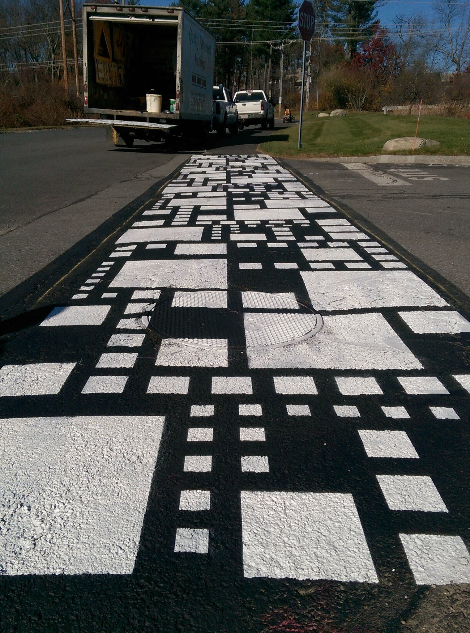 Black-and-white geometric pavement mosaic on a road, with a truck in the distance.