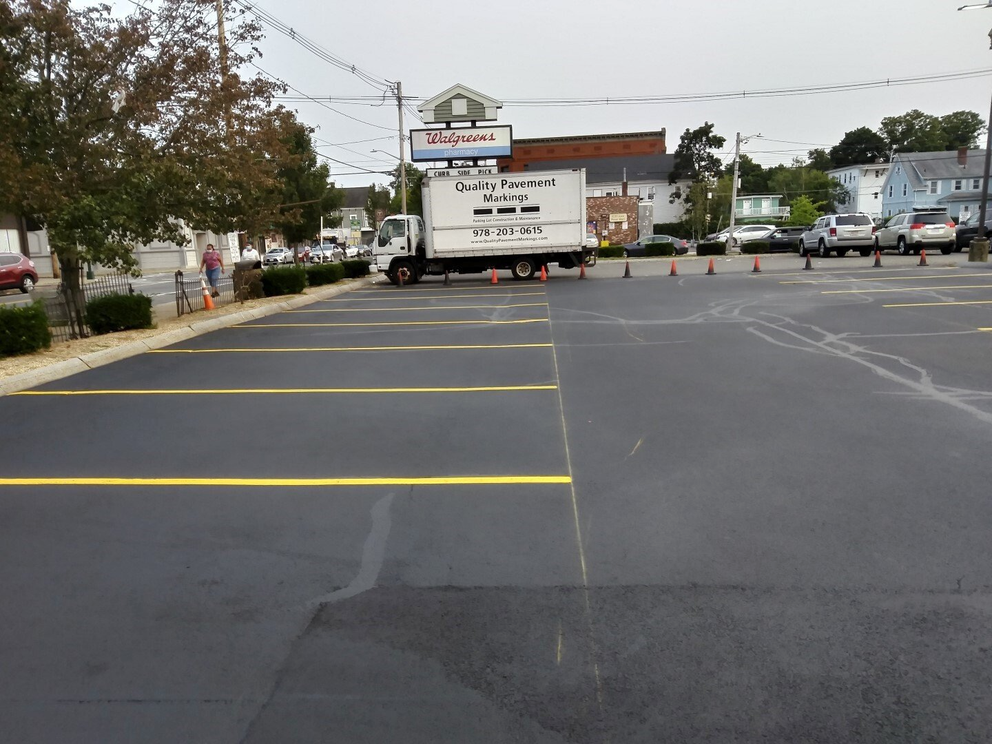 Empty parking lot with yellow lines and a white truck near a storefront under overcast skies
