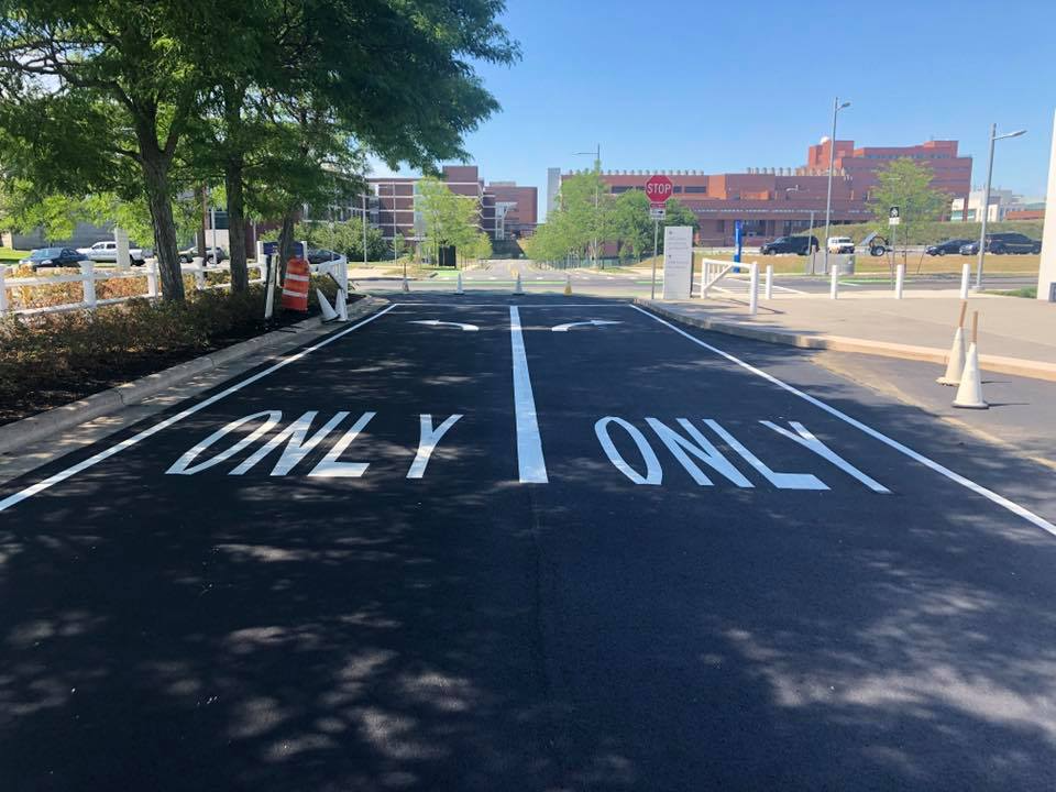 Parking lot lane with large white “ONLY” markings and cones beside a building under trees