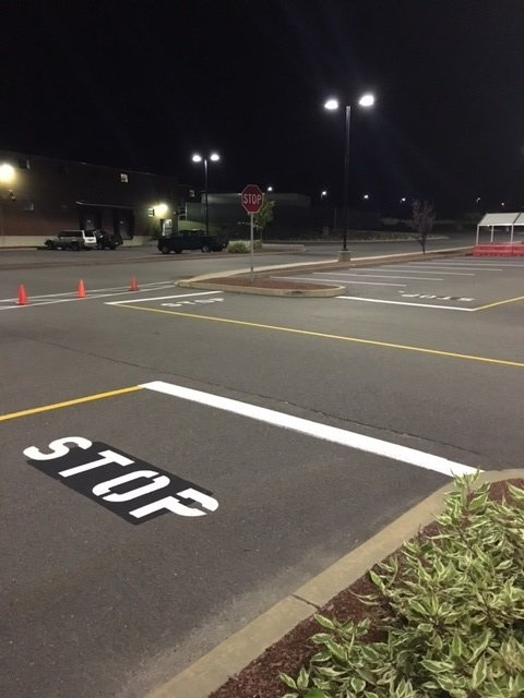 Empty parking lot at night with painted STOP marking, traffic cones, and a stop sign ahead