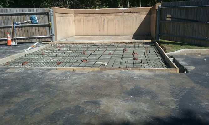 Concrete foundation slab with rebar grid in a fenced backyard, under construction