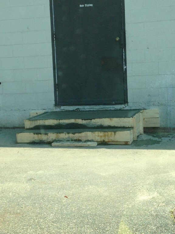 Black door above worn concrete steps against a white brick wall.