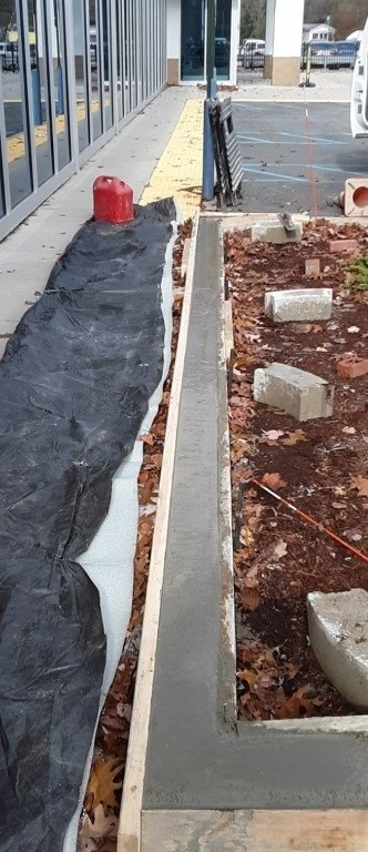Construction site walkway beside building with black tarp, red bucket, and curb edging