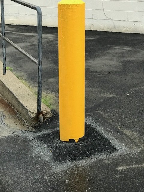 Yellow bollard beside a metal railing on wet asphalt near a building wall