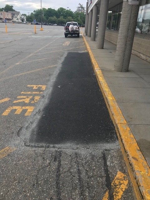 Parking lot curbside charging station with a car near a yellow curb and charging area marked “EV RIDE.”
