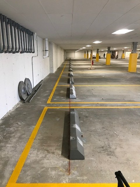 Empty parking garage with yellow lane markings, concrete wheel stops, and support columns.