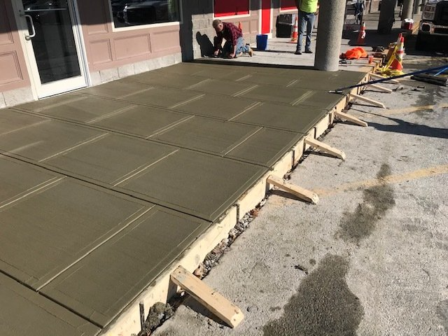 Fresh concrete walkway being leveled in front of a building during construction