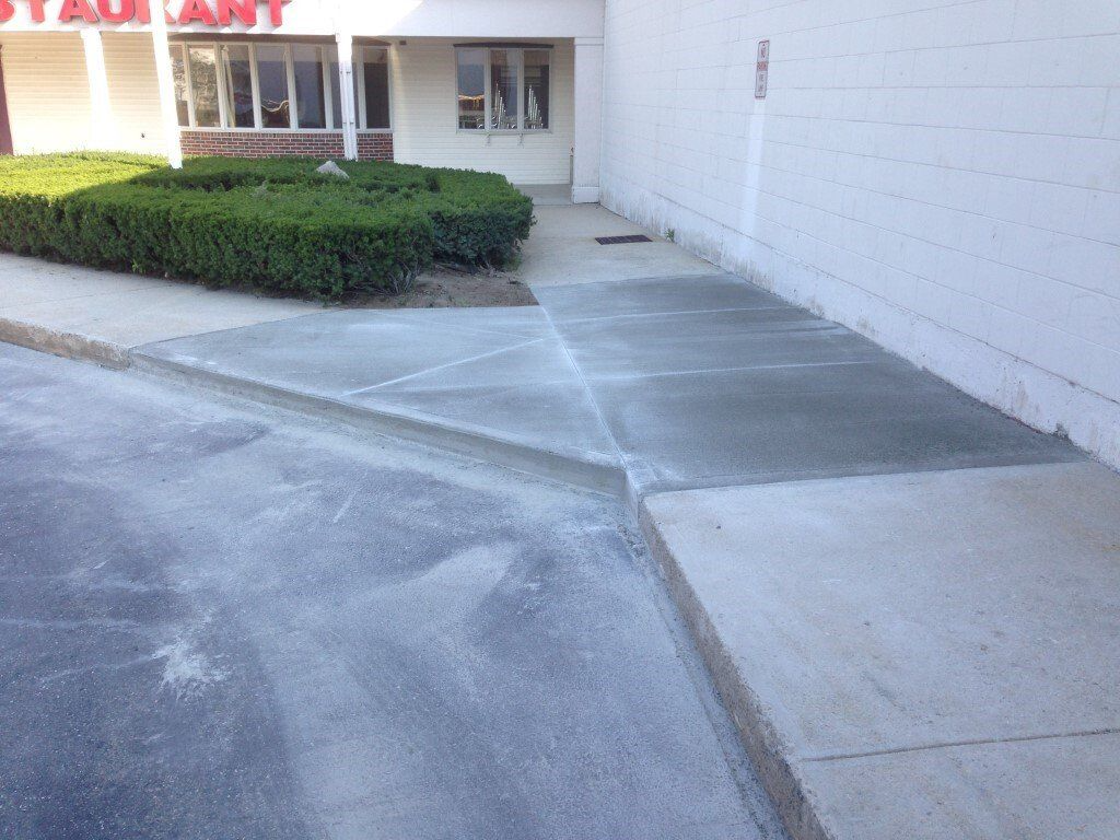 Empty concrete walkway beside a white building and trimmed hedge
