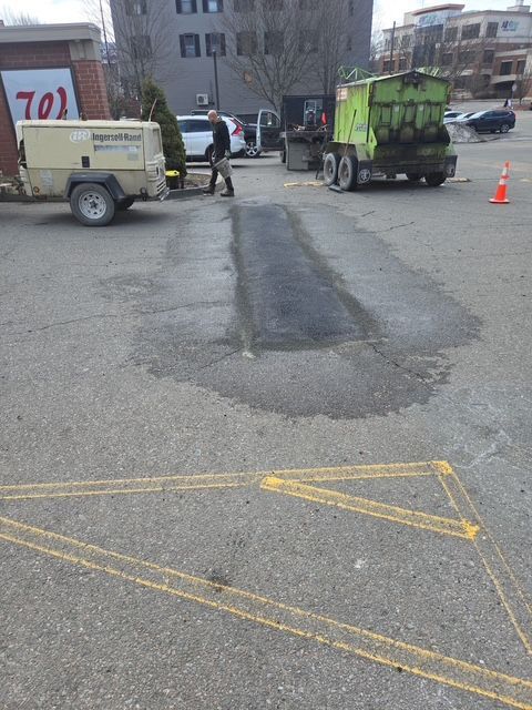 Two utility trucks and workers patching a road pothole, with cones marking the area.