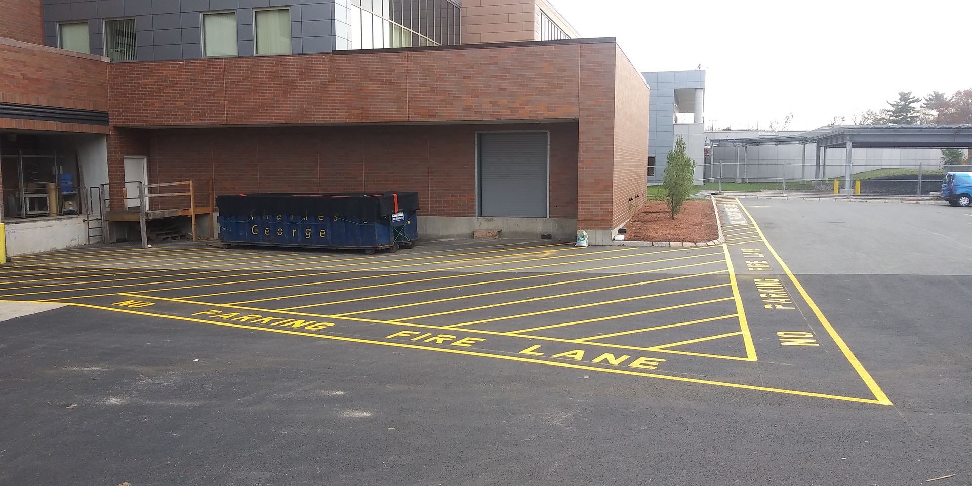 Empty parking lot with yellow crosshatch markings beside a brick industrial building