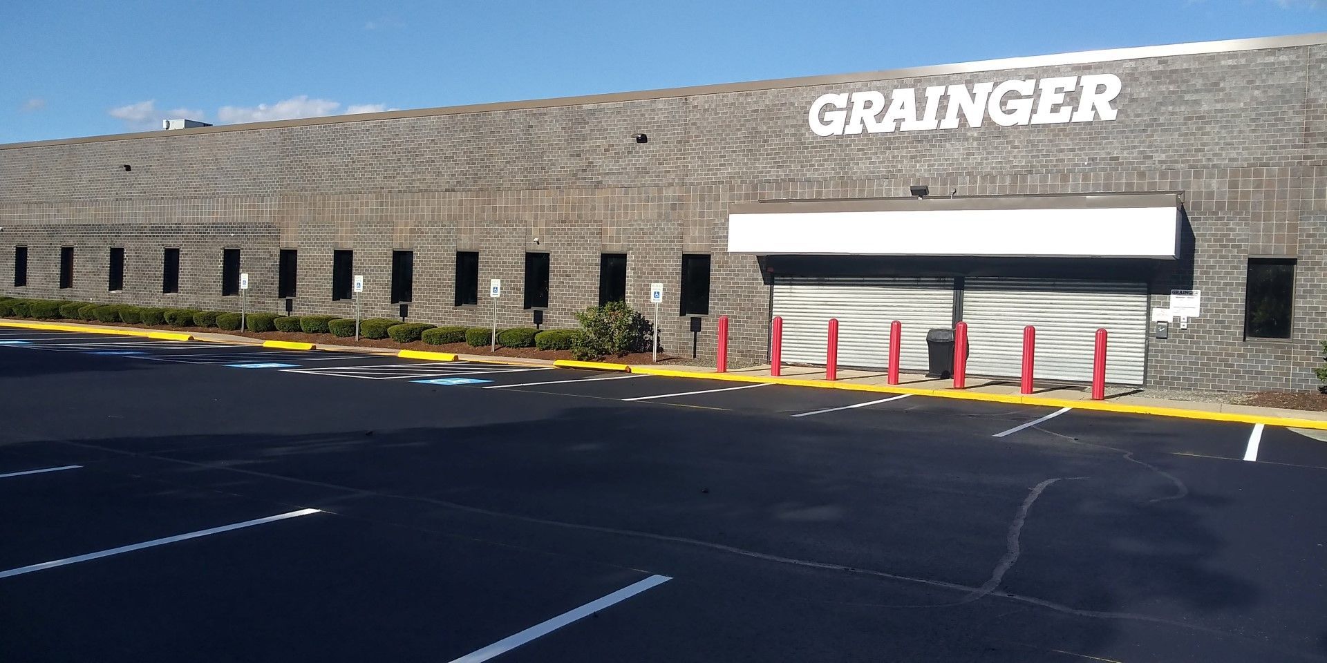 Grainger storefront with stone facade, white awning, red bollards, and empty parking lot