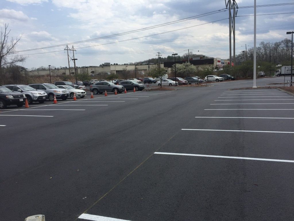 Empty parking lot with parked cars along the left and utility poles under a cloudy sky.