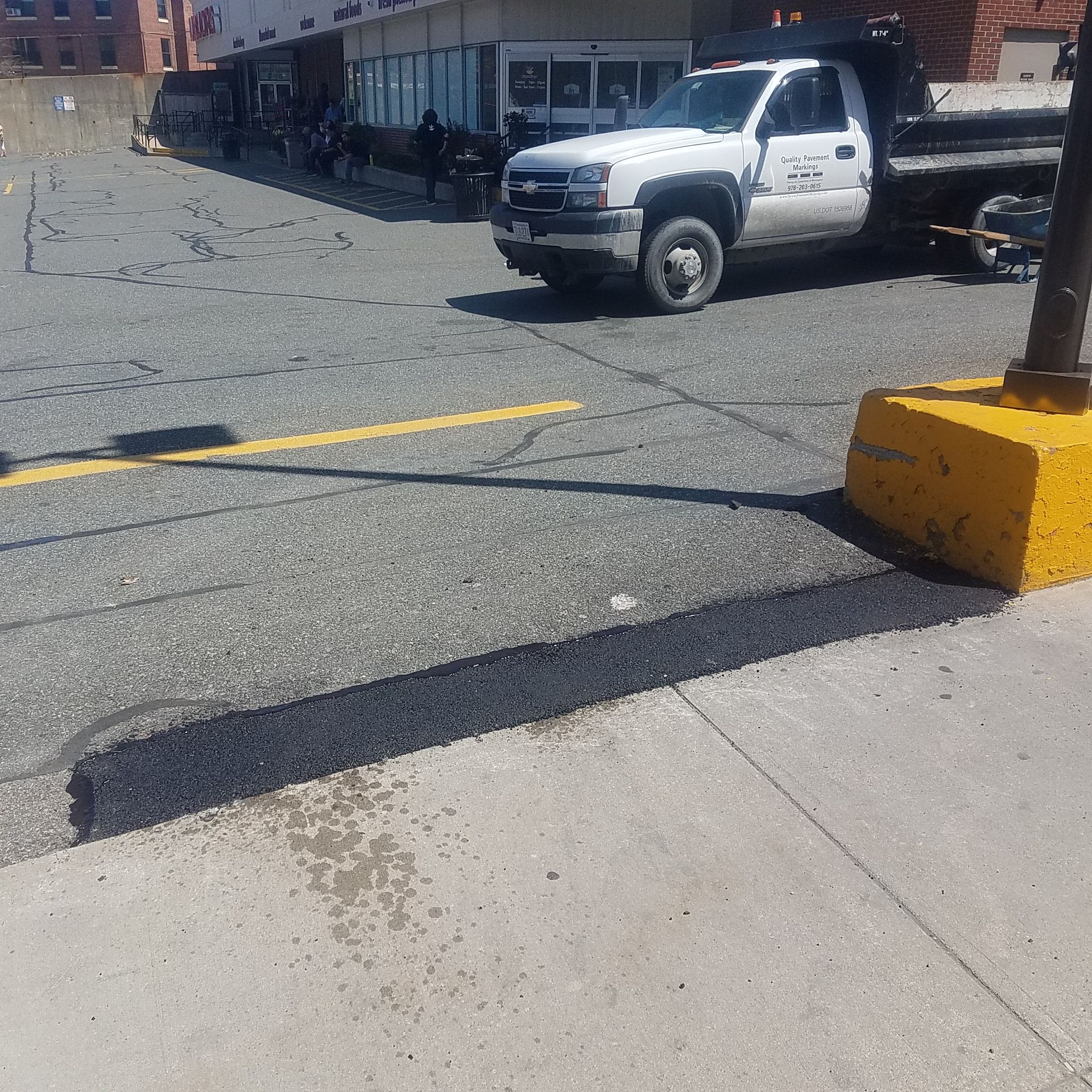 White pickup truck near a building beside a cracked parking lot with yellow painted lines and a curb stop