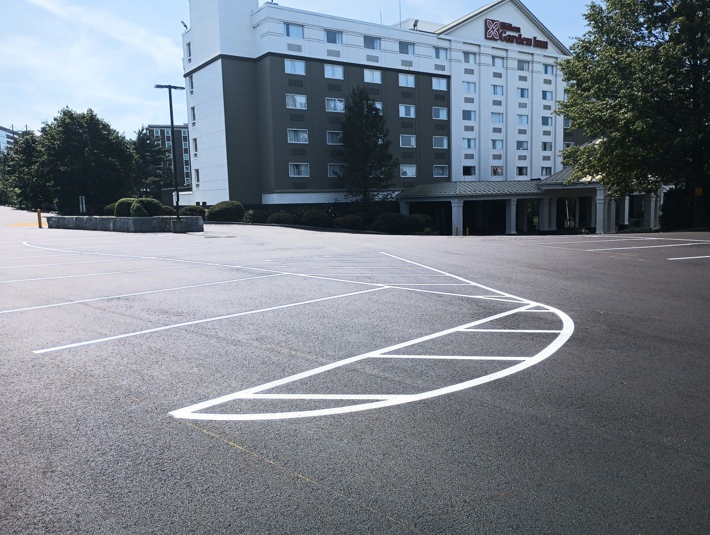 Empty outdoor parking lot in front of a multi-story building, with white court markings on the pavement