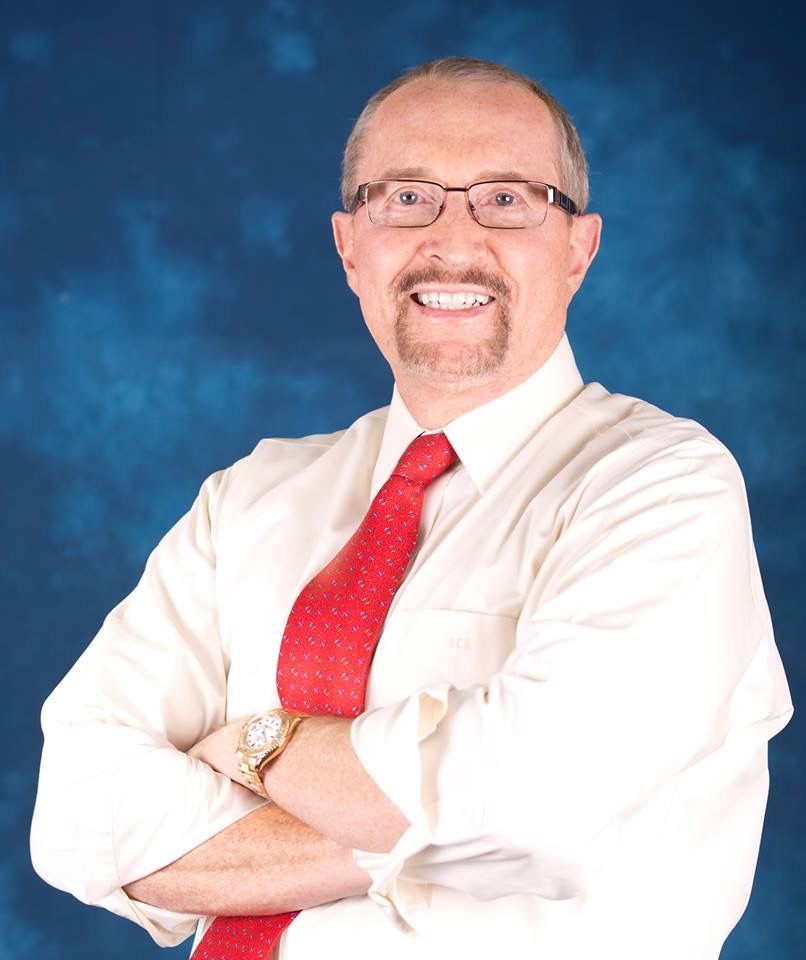 A man wearing glasses and a red tie is smiling with his arms crossed
