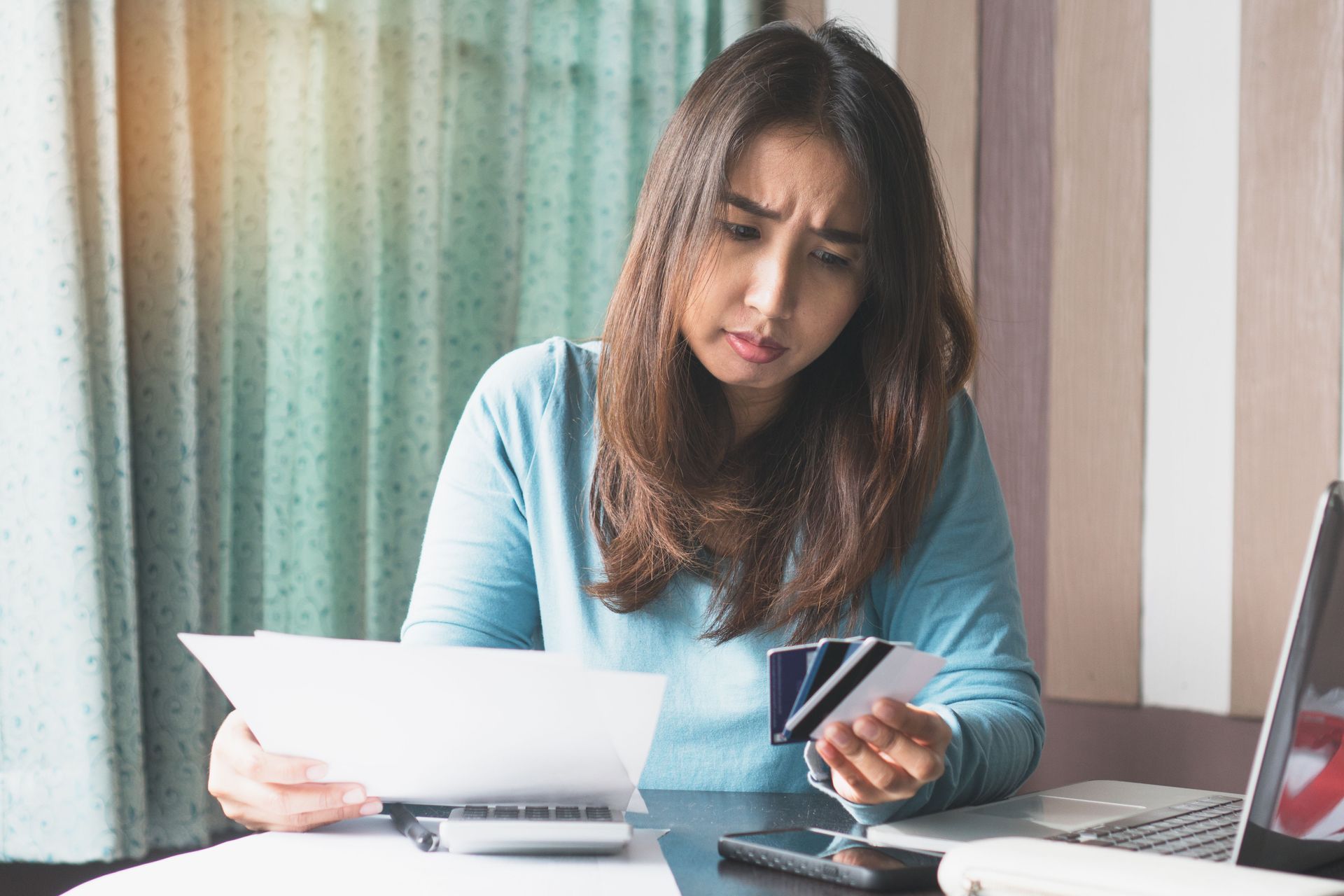 A woman is sitting at a table holding a credit card and a piece of paper.