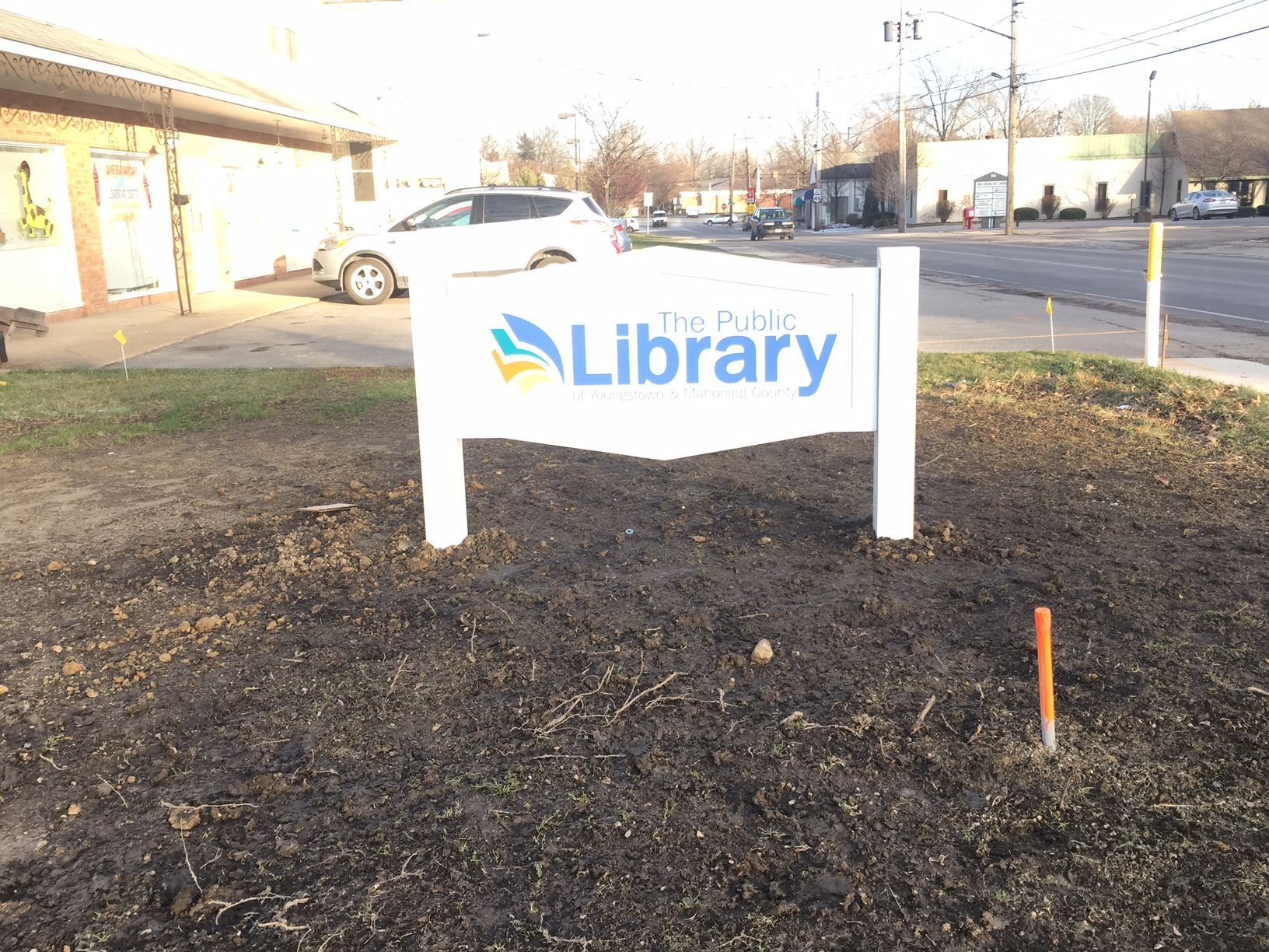 a library sign is sitting in the dirt in front of a building 