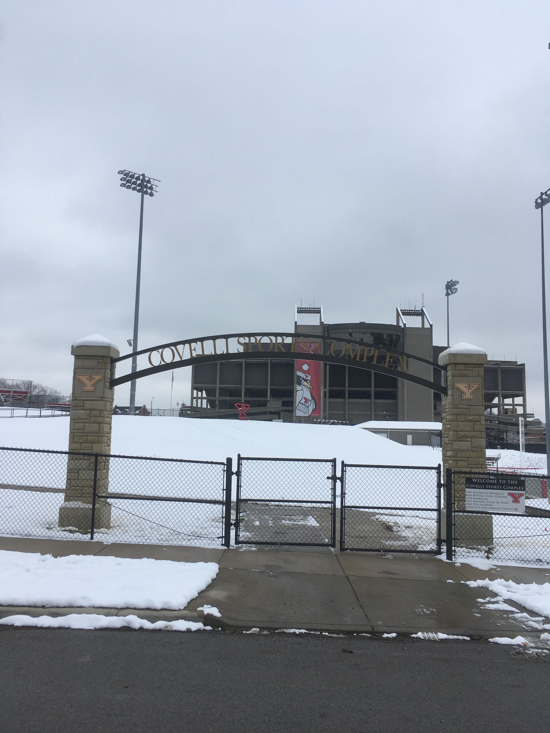 a fence surrounds a snowy field with a stadium in the background