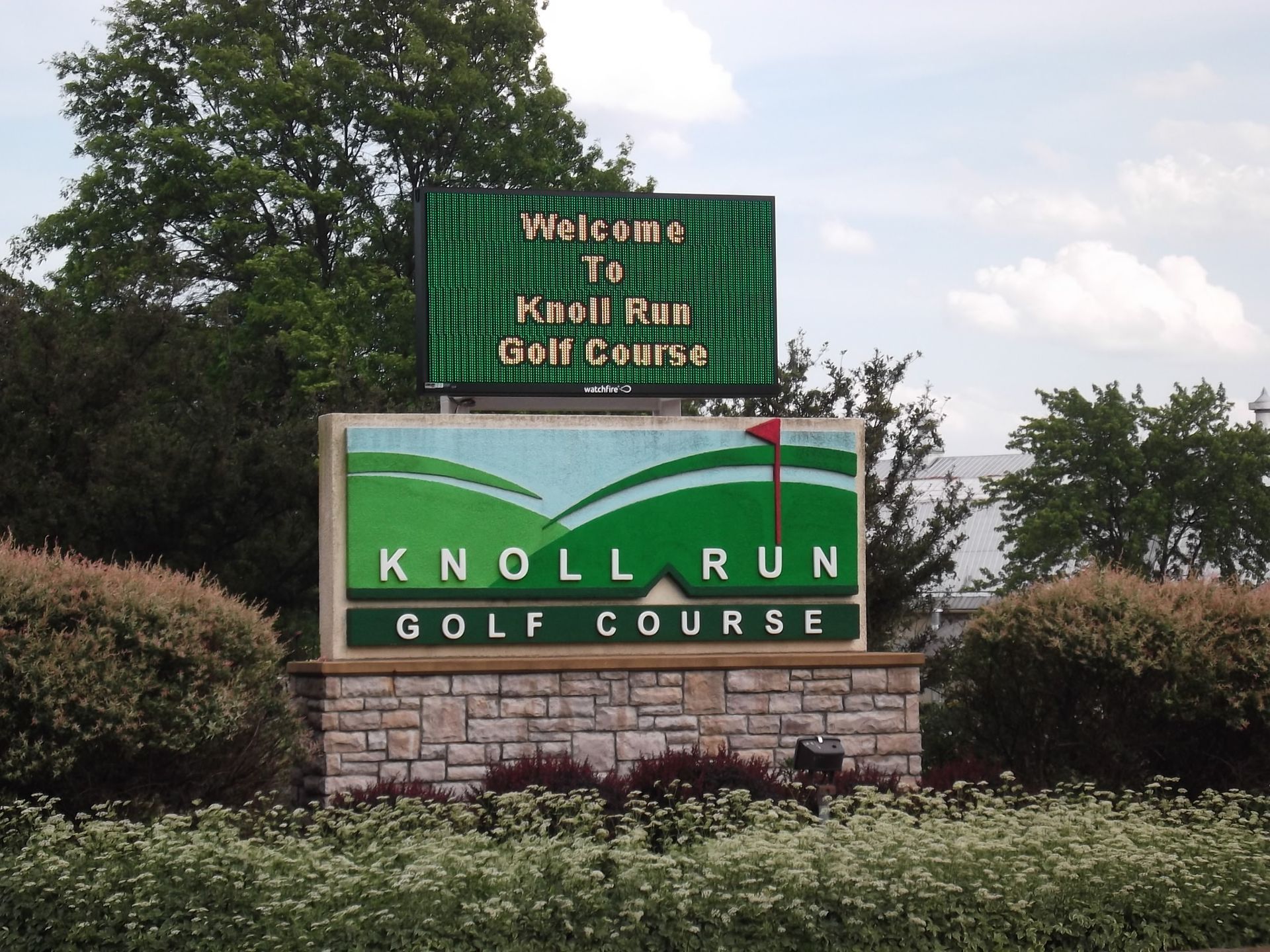 a sign for knoll run golf course is surrounded by bushes
