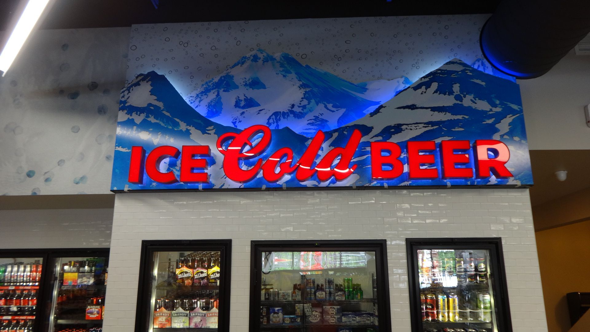 ice cold beer sign with red letters and blue and white mountains as a background