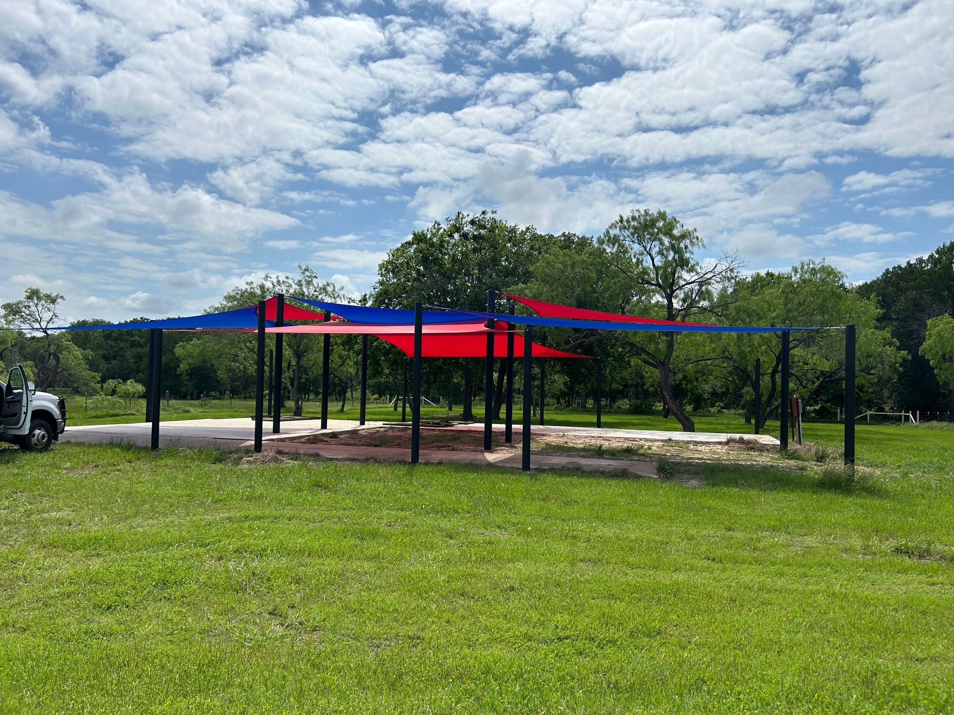 A red , blue and white umbrella is sitting in the middle of a grassy field