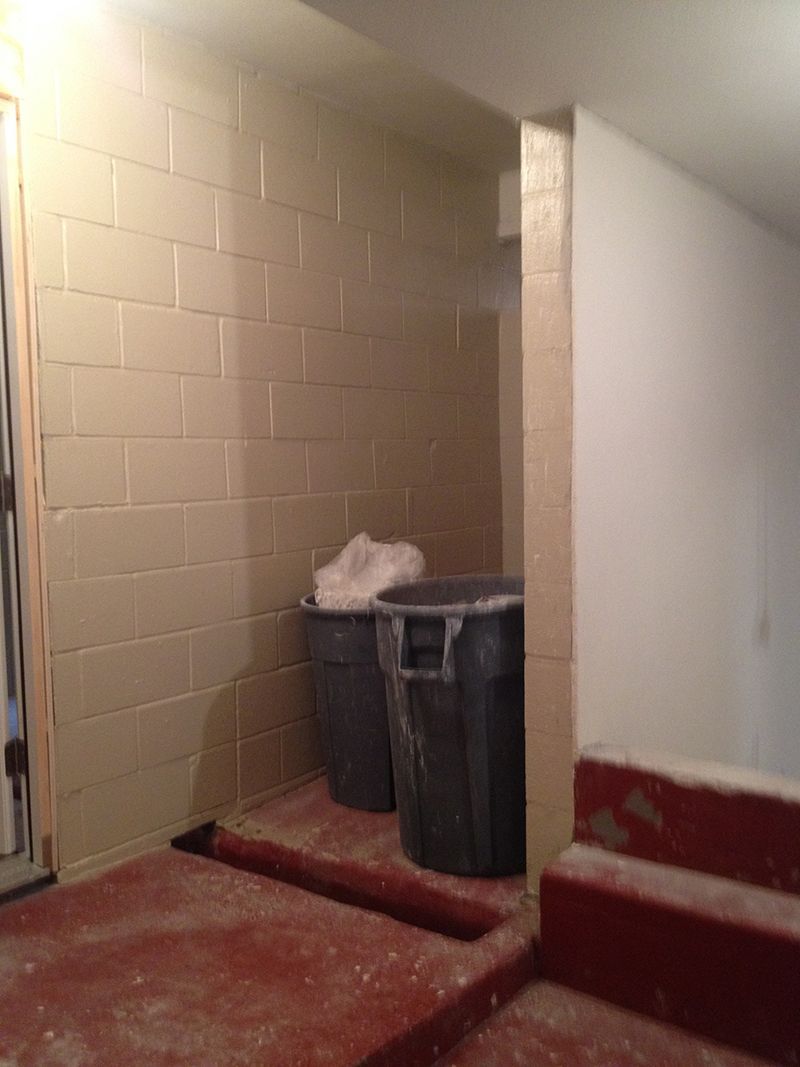 A room with a brick wall and two trash cans on the floor.