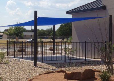 A blue shade sail is attached to a pole in front of a building