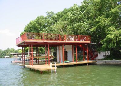 A dock with a red railing is in the middle of a lake surrounded by trees.