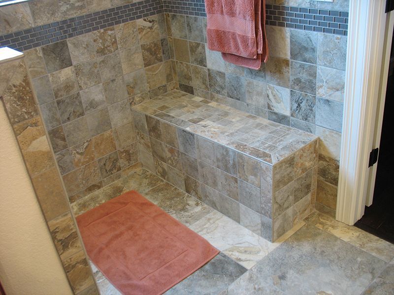 A bathroom with tiled walls and a bench in the shower.