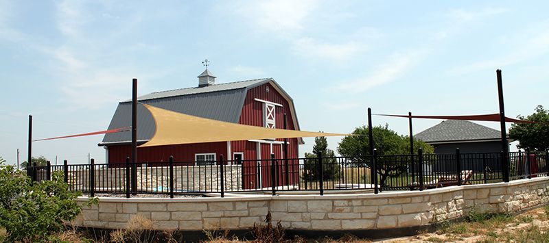 A red barn is surrounded by a stone wall and a fence.