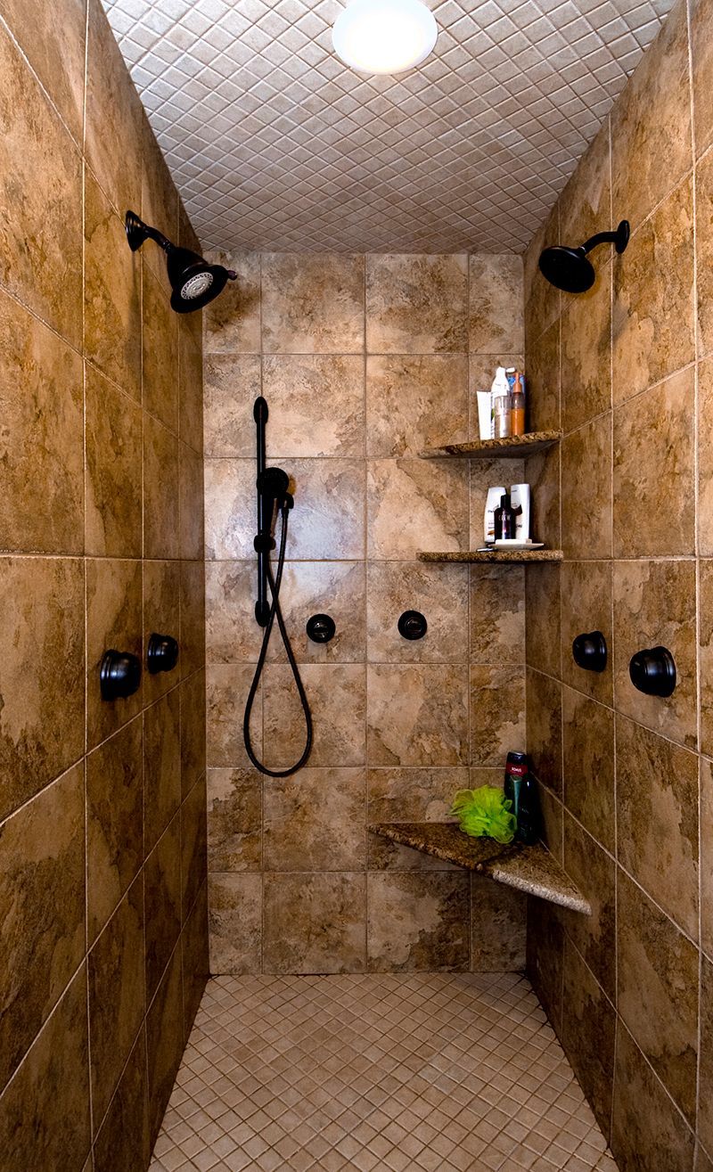 A walk in shower with two shower heads and a bench.