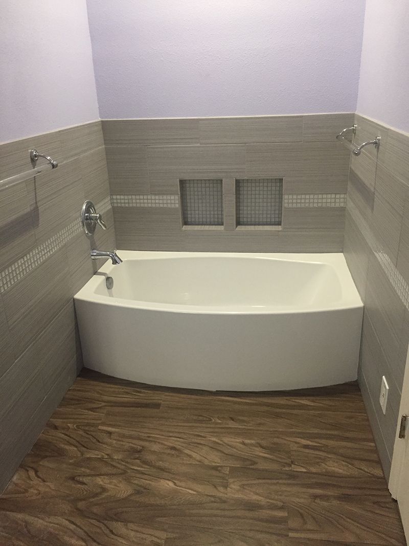 There is a bathtub in the bathroom with a wooden floor.