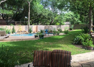 There is a swimming pool in the backyard with a bench in the foreground.