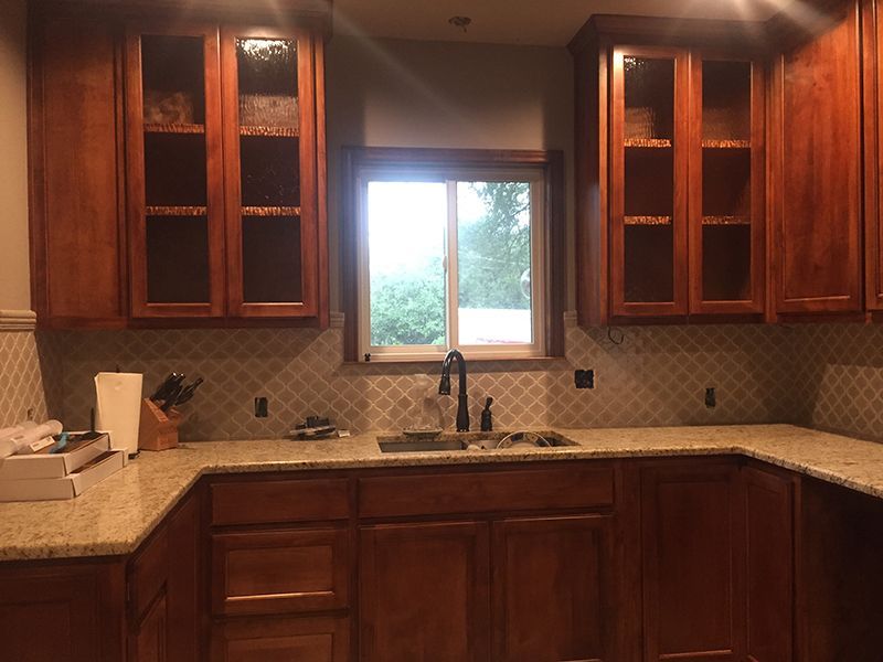 A kitchen with wooden cabinets , granite counter tops , a sink and a window.