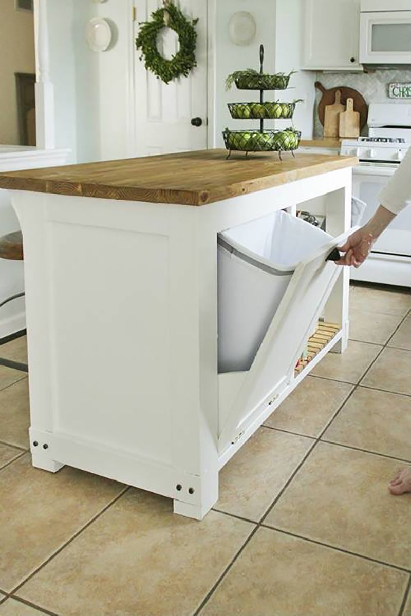 A person is putting a trash can into a kitchen island.