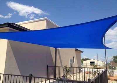 A blue shade sail is hanging over a fence in front of a house.