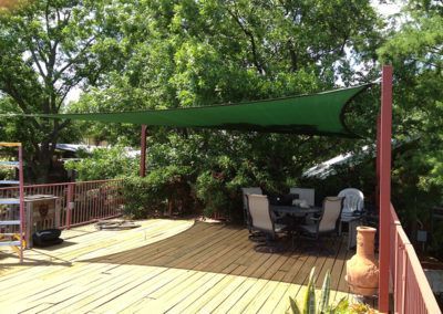 A deck with a table and chairs under a green umbrella.