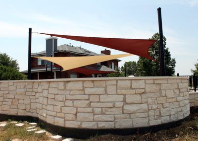 A stone wall with three shade sails on it in front of a house.