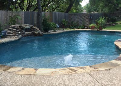 A large swimming pool with a waterfall in the backyard.