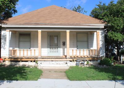 A white house with a brown roof and a porch.