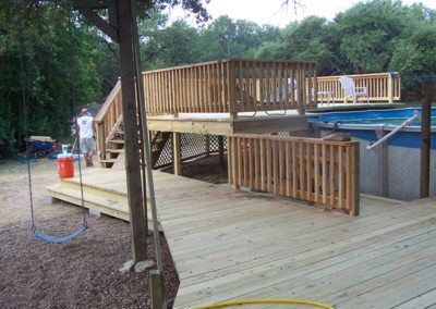 A man is standing on a wooden deck next to a pool.