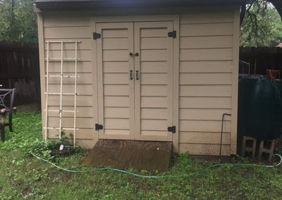 A small white shed is sitting in the middle of a grassy yard.