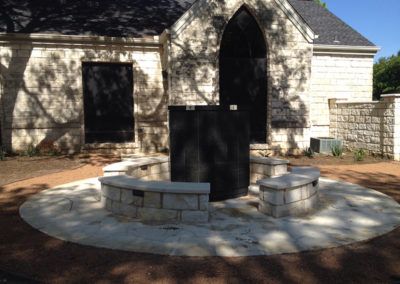 A white building with a black door and a stone patio in front of it.