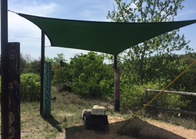 A green shade sail is hanging from a pole in a field.