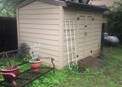 A shed in a backyard with a bench and potted plants.