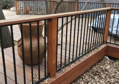 A wooden deck with a metal railing and a pot on it.
