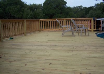 A wooden deck with chairs and a table next to a pool.