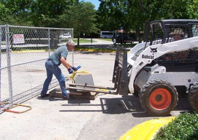 A man is pushing a bobcat forklift in a parking lot